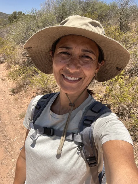 A hiker’s selfie on a dry trail, in a sun hat and backpack.