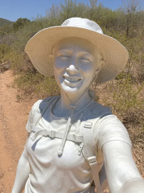 The same hiker as a white marble statue, hat and backpack included.